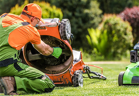 Man kneeling down doing maintenance on a commercial lawnmower